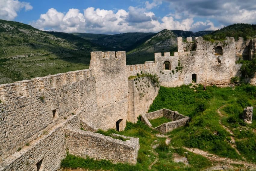 "Tvrđava Blagaj iznad izvora Bune, okružena planinskim pejzažima."