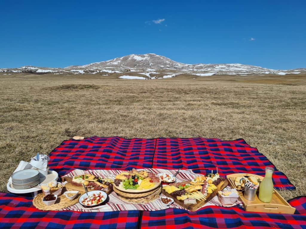 Planinski piknik na Livanjskom polju s pogledom na planinu Cincar, uz bogatu hranu, tradicionalne specijalitete i prostrane prirodne pejzaže.