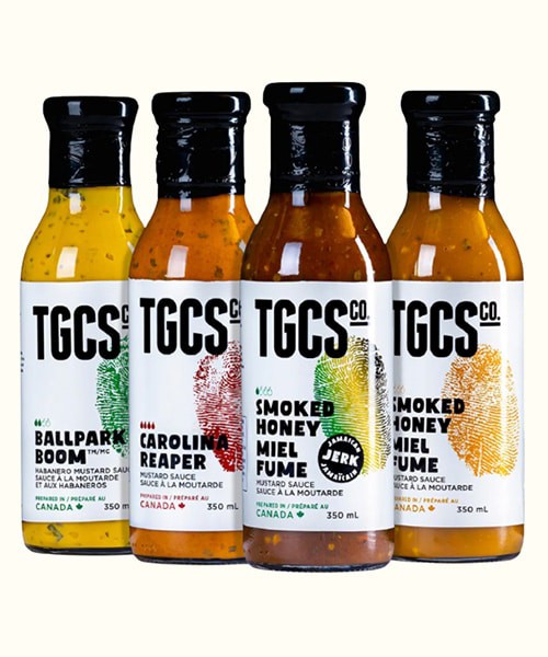 Vibrant selection of craft BBQ sauces from TGCS Co. featuring unique flavors like Ballpark Boom, Carolina Reaper, Smoked Honey, and Maple Honey, each in 350ml bottles.
