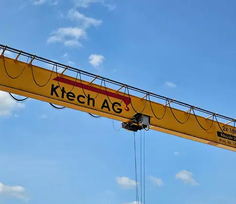 Gelber Industriekran mit Ktech AG Logo unter blauem Himmel.