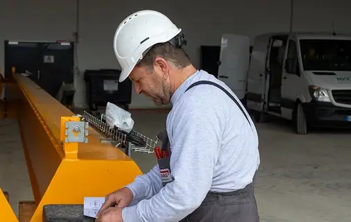 Mann mit Schutzhelm prüft Industriekran in Werkstatt.