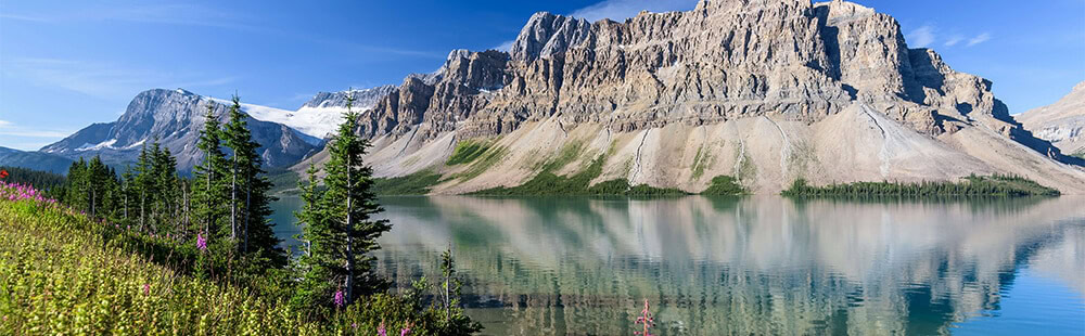 Majestic mountain lake with cliffs, evergreen trees, and clear blue sky.
