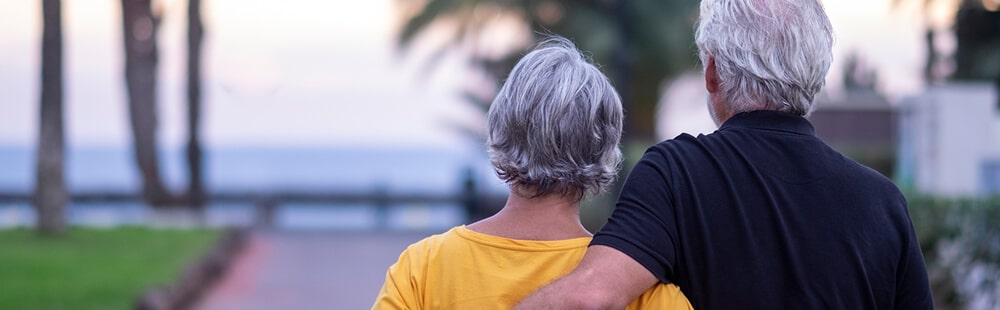 Elderly couple enjoying a sunset by the water, embracing and relaxing outdoors.