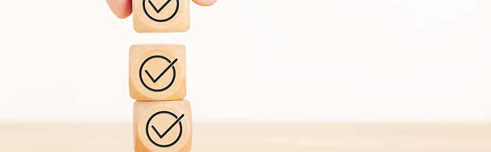 Hand stacking wooden blocks with checkmarks, symbolizing organization and task completion.