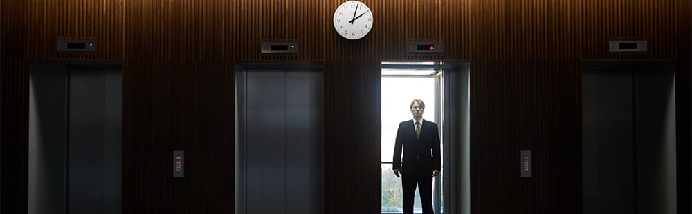 Business professional waiting in elevator lobby with wooden walls and clock.