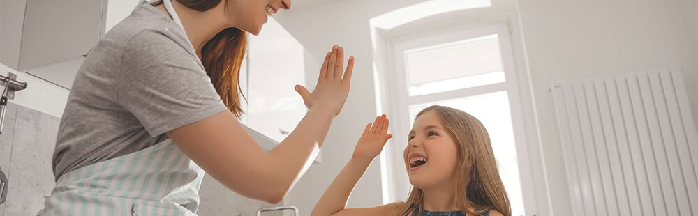 Mother and daughter sharing a joyful high five in the kitchen.