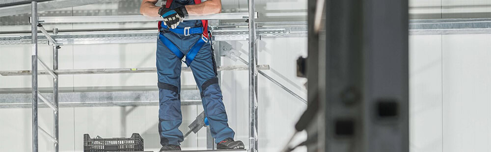 Worker wearing safety harness on scaffolding at construction site.