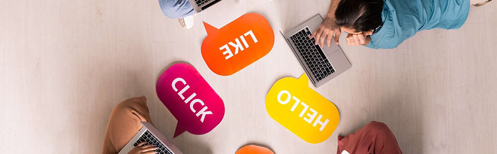 Group of diverse people working together with laptops and speech bubbles on a light wooden table.