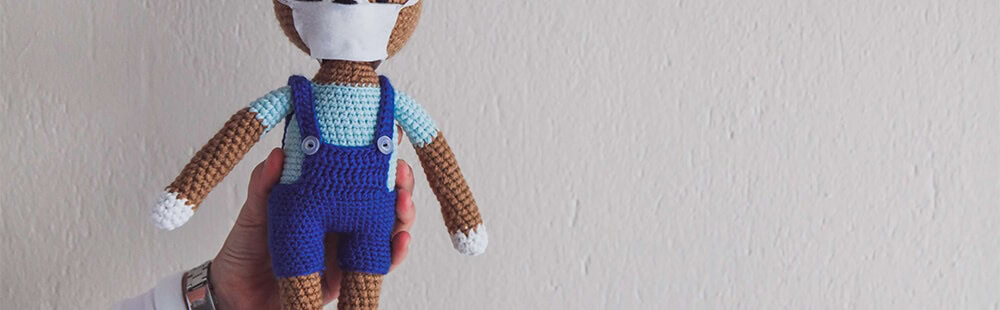 Knitted doll with blue overalls, white hat, and brown skin tone.