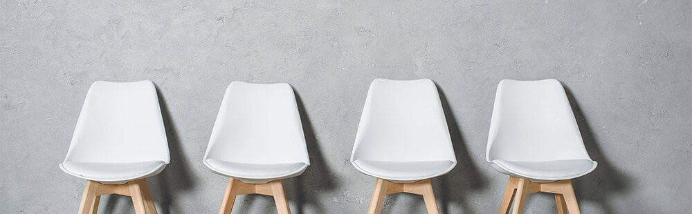 White modern chairs with wooden legs arranged in a row on grey background.
