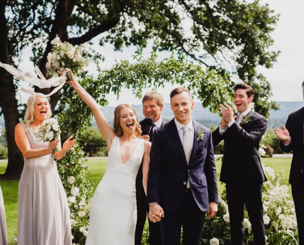 A joyful bride and groom celebrate their outdoor wedding at Scholls Valley Lodge, surrounded by happy bridesmaids and groomsmen.