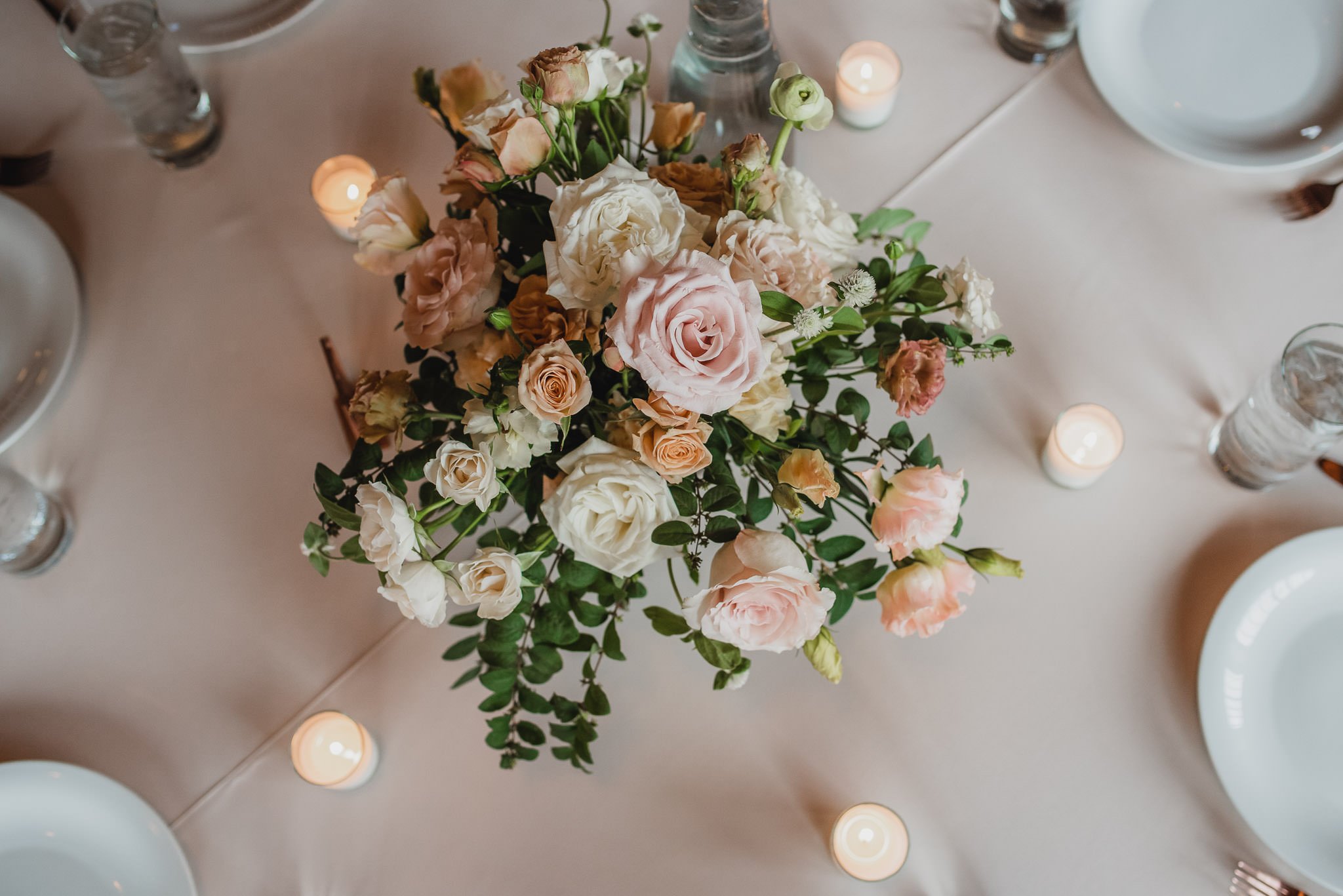 Capture the elegance of wedding photos at Castaway Portland with a top view of a floral centerpiece featuring pink and white roses, surrounded by small lit candles and plates.