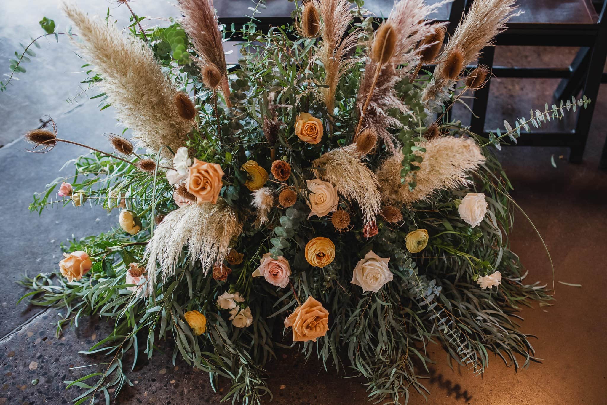 A floral arrangement featuring pampas grass, roses, and greenery beautifully complements wedding photos at Castaway Portland, all set against a dark floor.