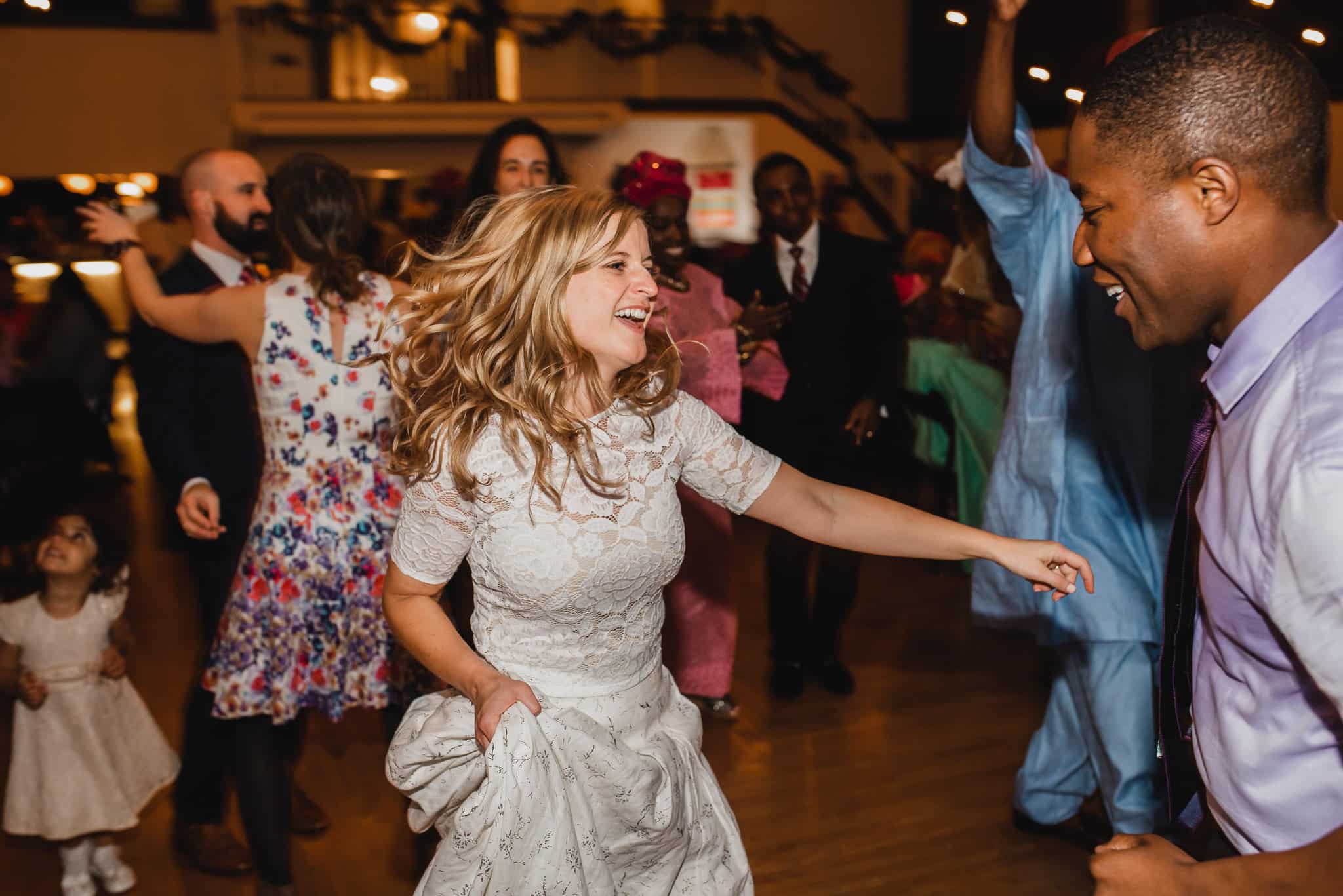 At a lively wedding at the Evergreen, people are dancing joyfully, with a woman in a white dress and a man in a tie leading the dance.