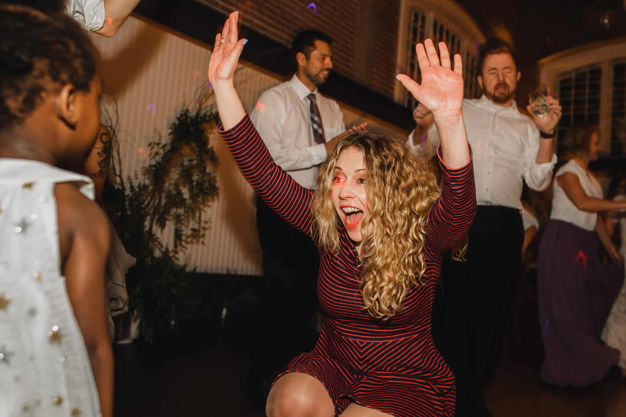 At the Evergreen wedding, a woman in a red striped dress dances energetically, surrounded by several people in a lively setting.