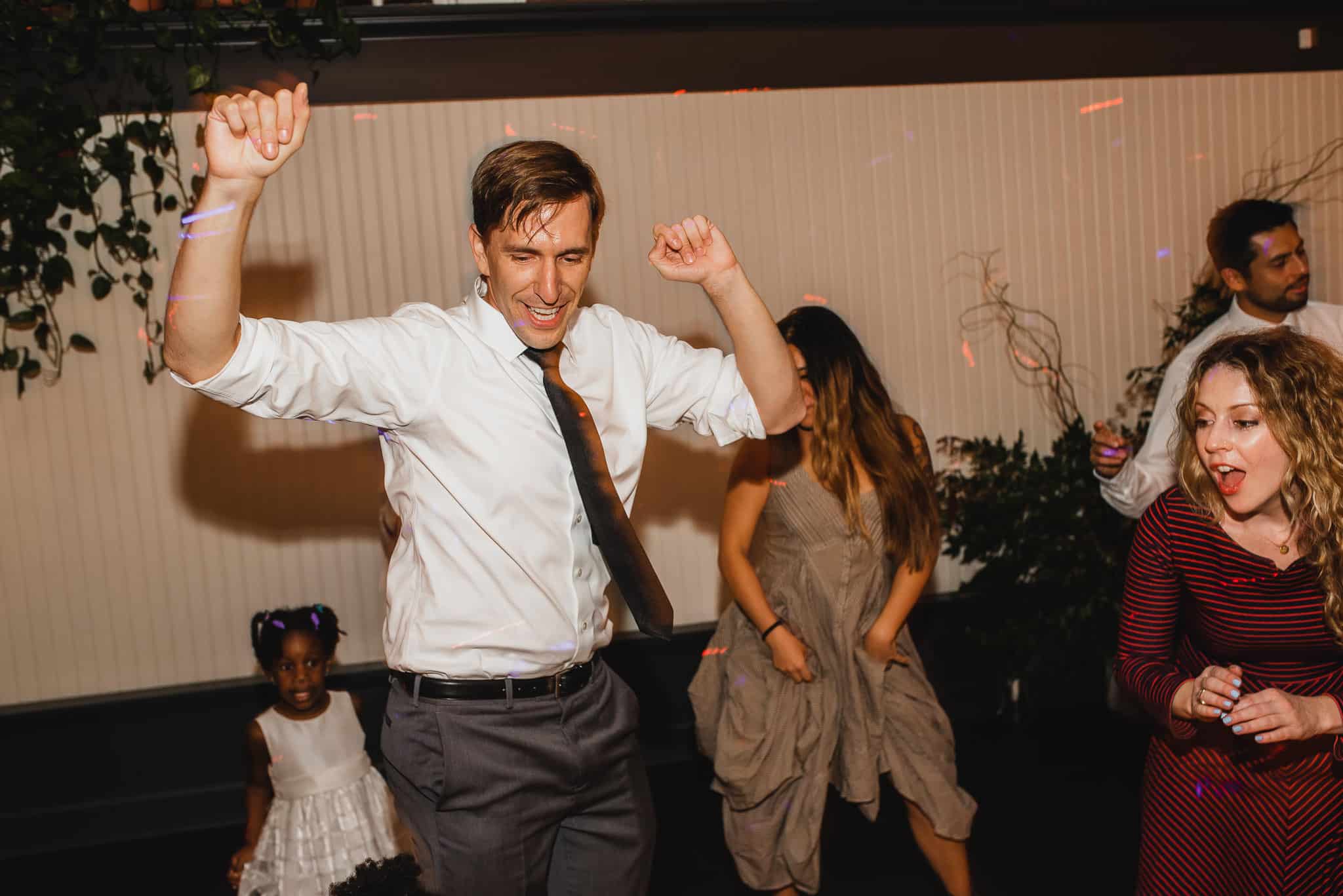 At the Evergreen wedding, people danced energetically, with a man in a tie raising his arms and others smiling and enjoying the music.