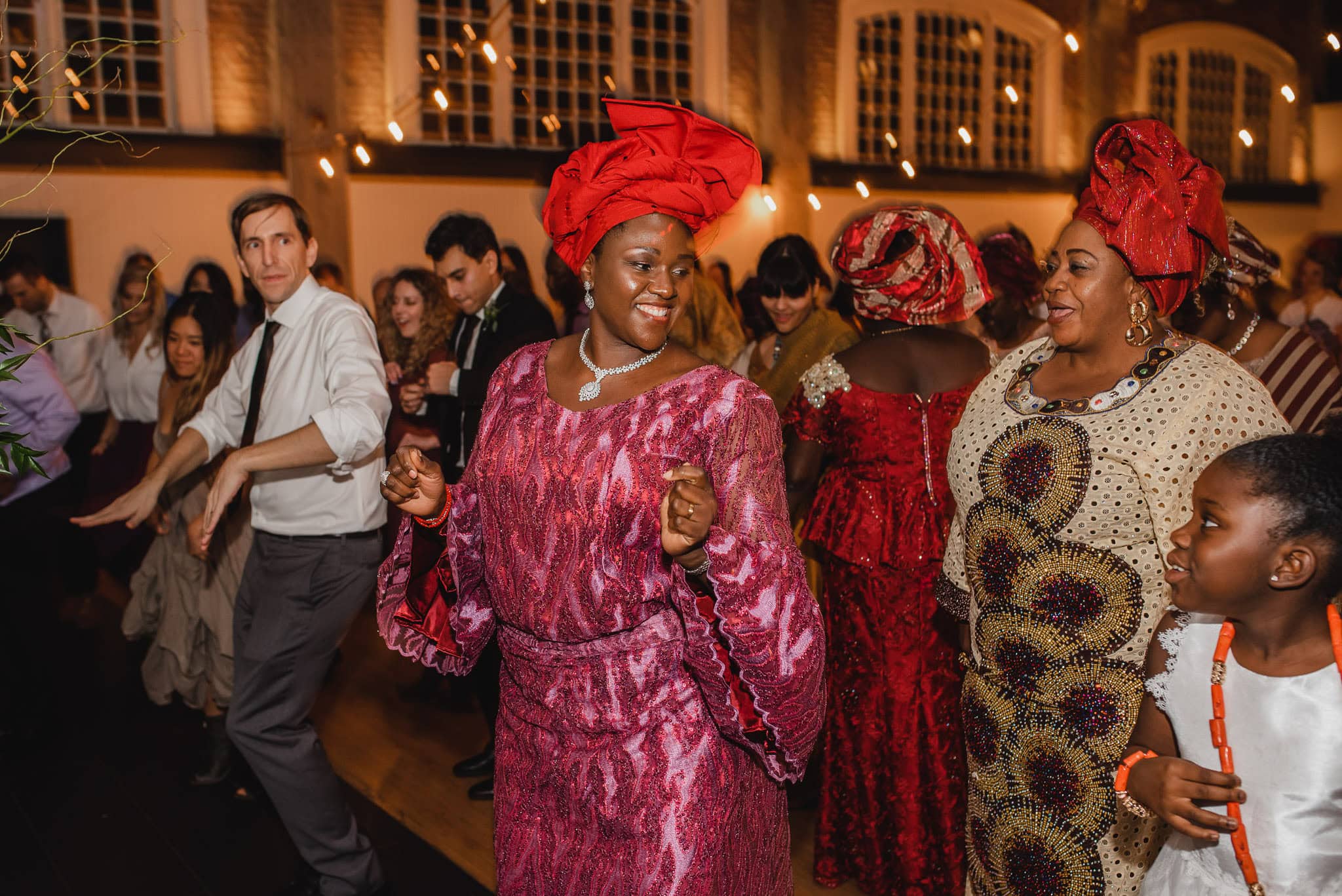 At a lively wedding at the Evergreen, people joyfully dance in vibrant traditional attire under warm lighting, creating a festive atmosphere.