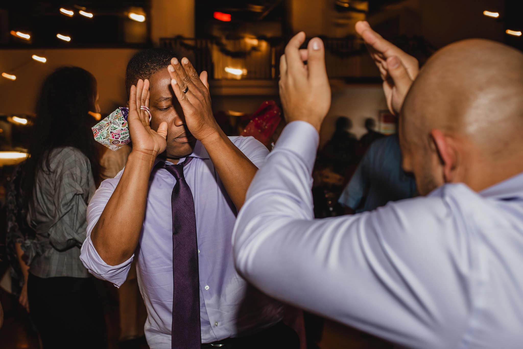 Two men dancing energetically at a wedding at the Evergreen, surrounded by others in a dimly lit room.
