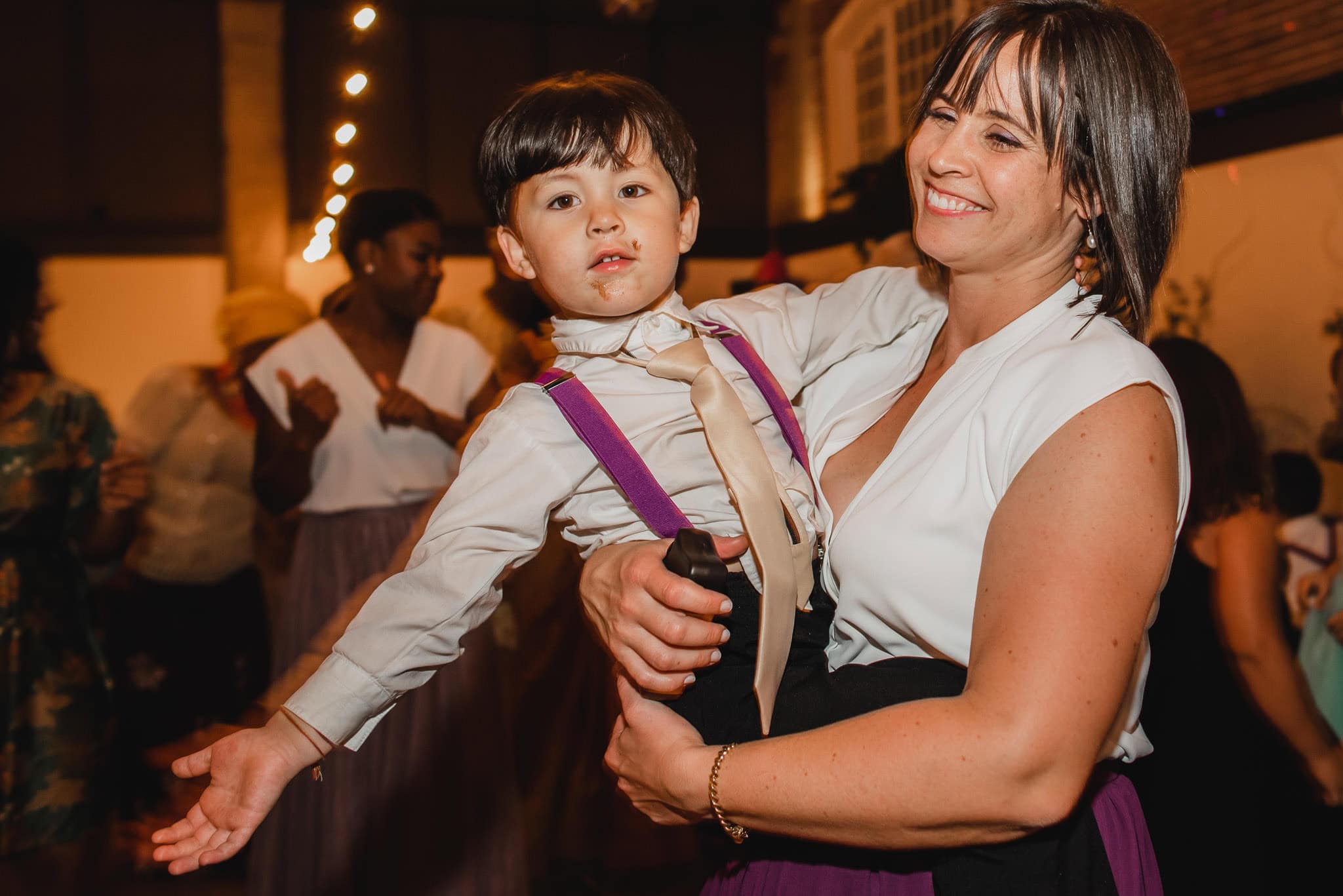 A woman beams as she holds a young boy in her arms at a lively indoor wedding at the Evergreen.