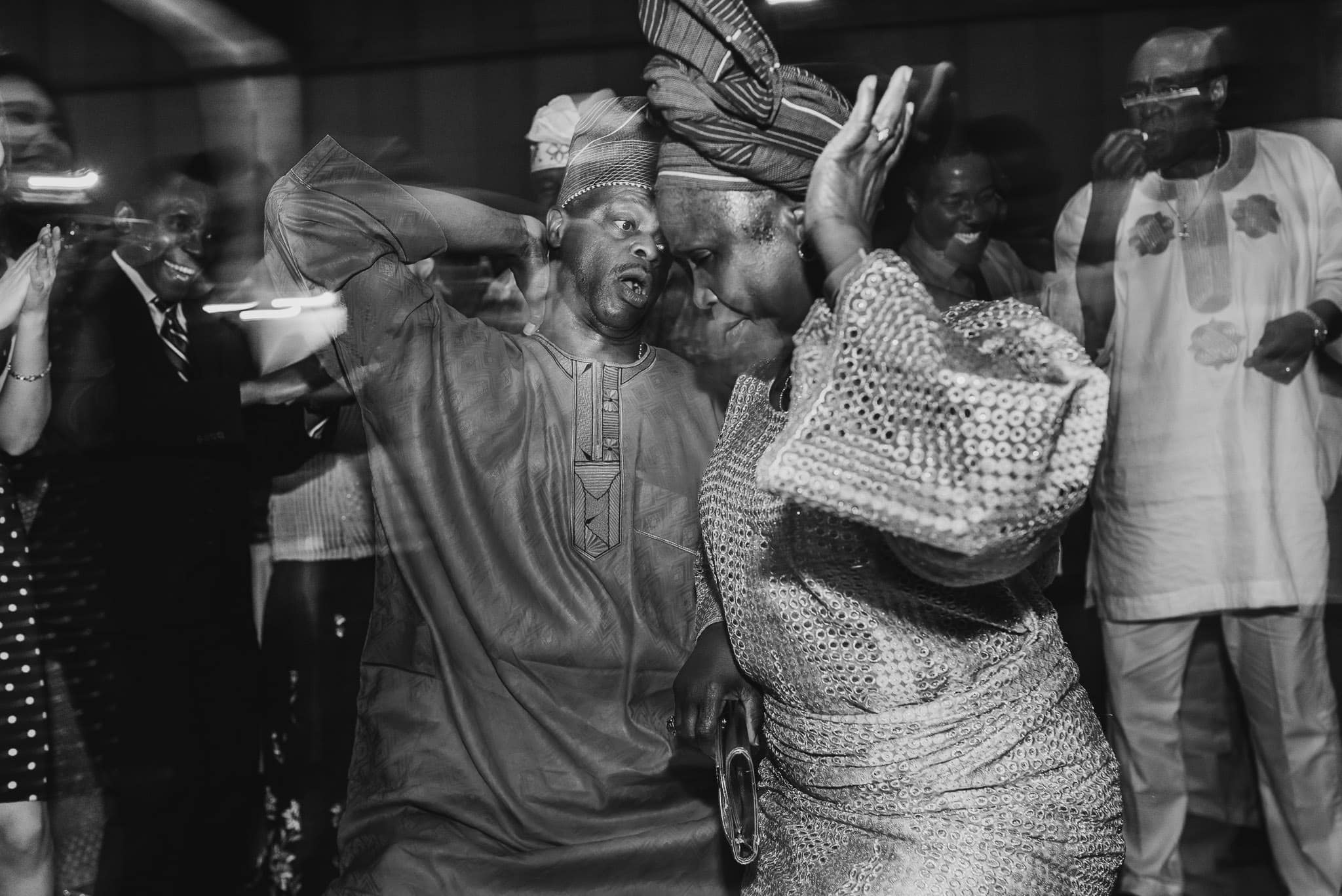 Two people in traditional attire dance energetically at a lively wedding at the Evergreen, surrounded by applauding onlookers.