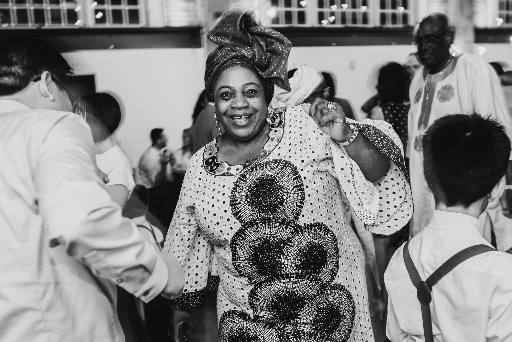 A woman in a patterned dress and headwrap dances joyfully at a lively wedding at the Evergreen gathering.