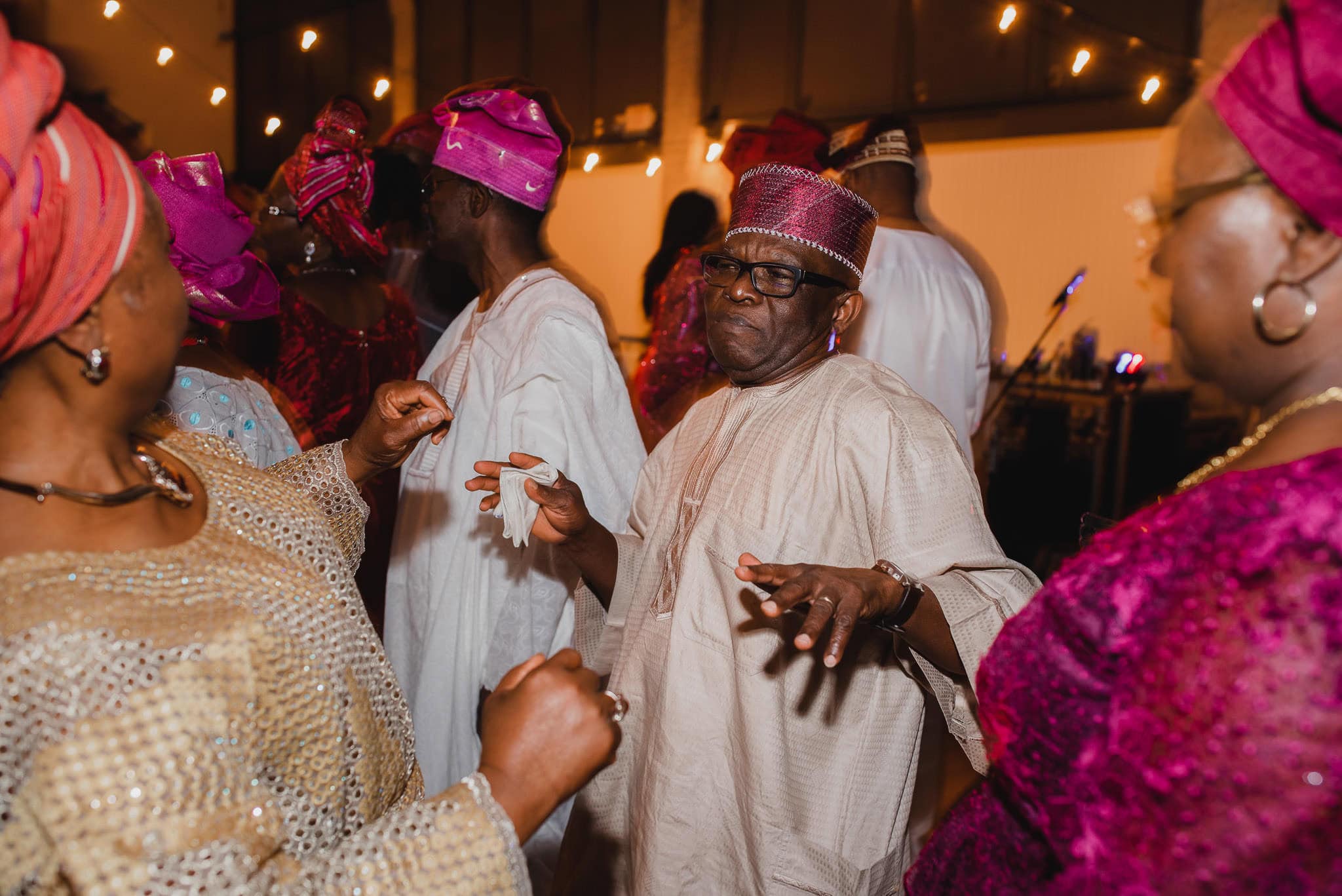 People in colorful traditional attire are joyfully dancing indoors, celebrating a wedding at the Evergreen.