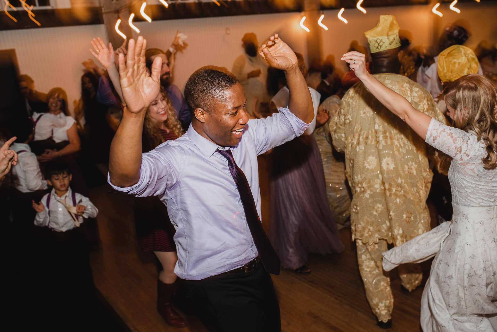 A man in a dress shirt and tie dances joyfully among a group of people at a wedding at the Evergreen indoor event.