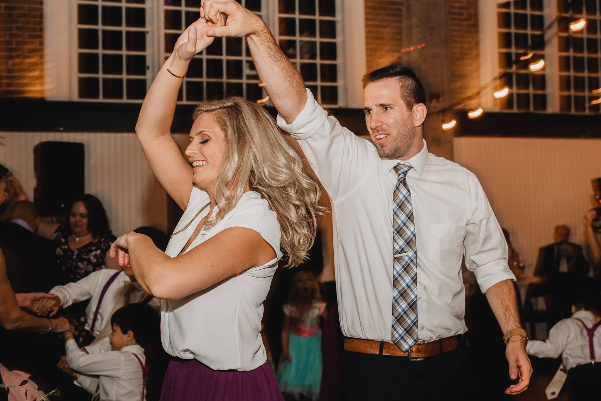 A man and woman dance together at the Evergreen, smiling and holding hands in celebration of a joyful wedding event indoors.
