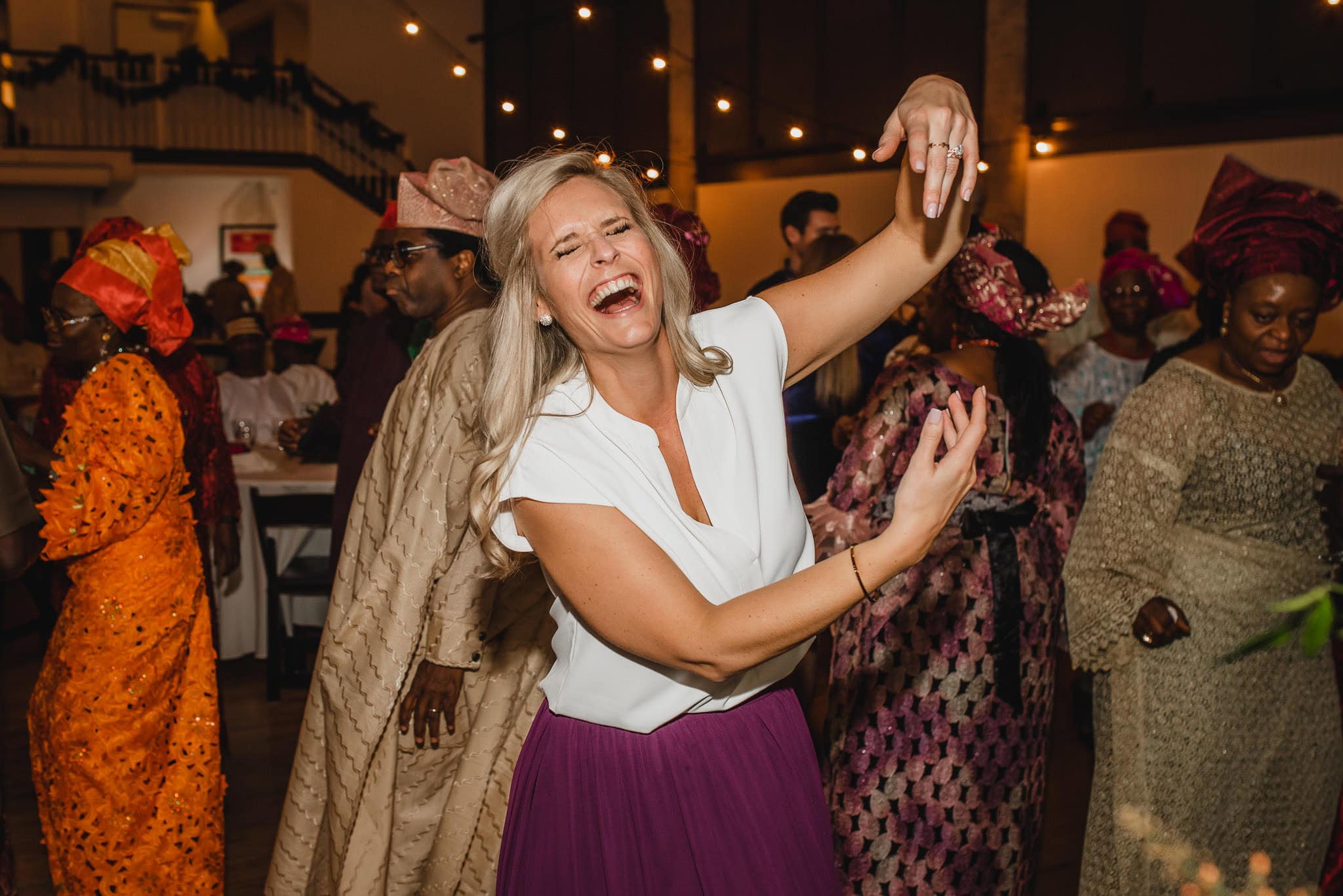 A joyful woman dancing at an indoor celebration, surrounded by people in colorful traditional attire at a wedding at the Evergreen.