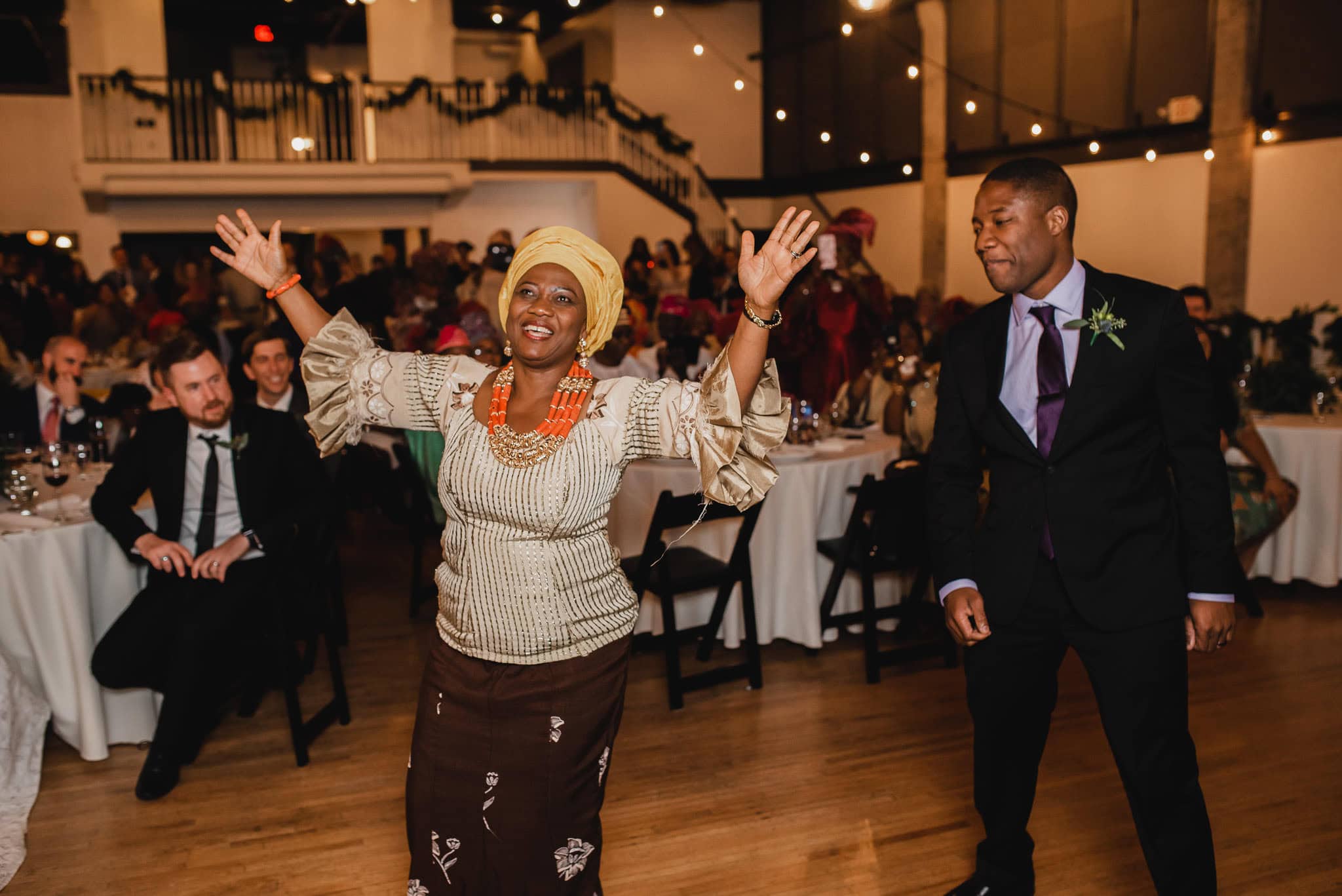 A woman dances joyfully at the wedding at the Evergreen, with guests seated at tables in the background.
