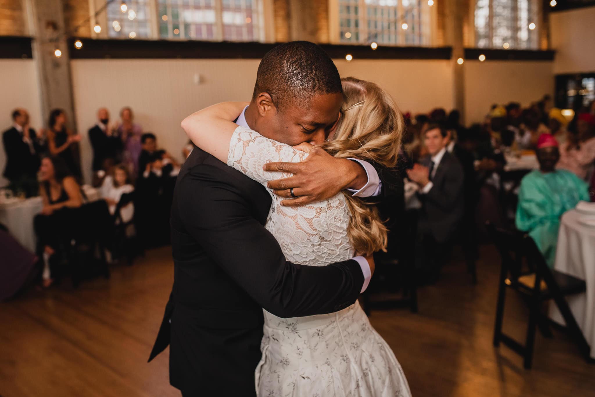 A couple embraces on the dance floor at the wedding at the Evergreen, with guests seated in the background.
