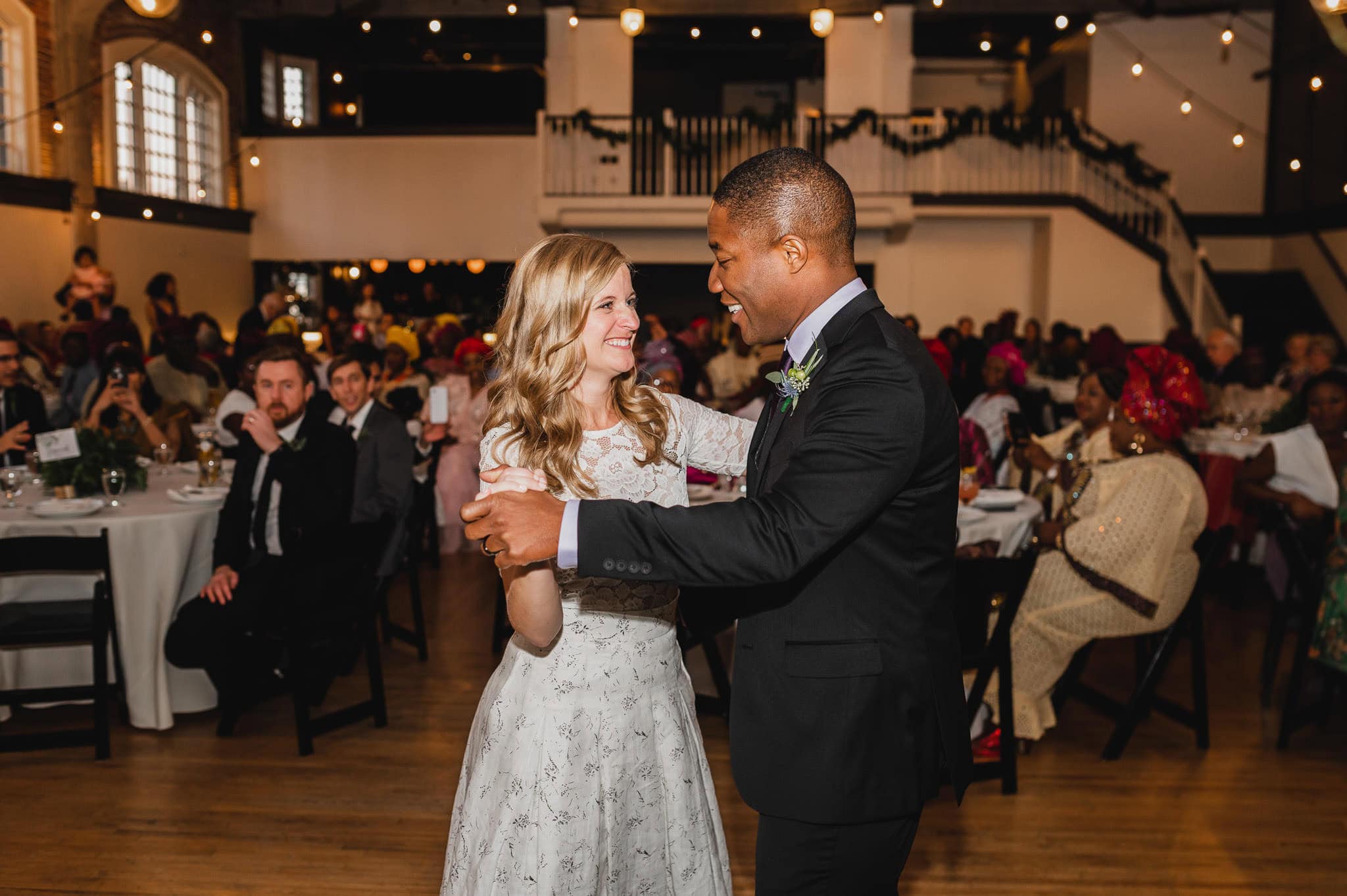 At the Evergreen, a couple dances joyfully at their wedding reception, surrounded by warmly lit tables of guests celebrating their love.