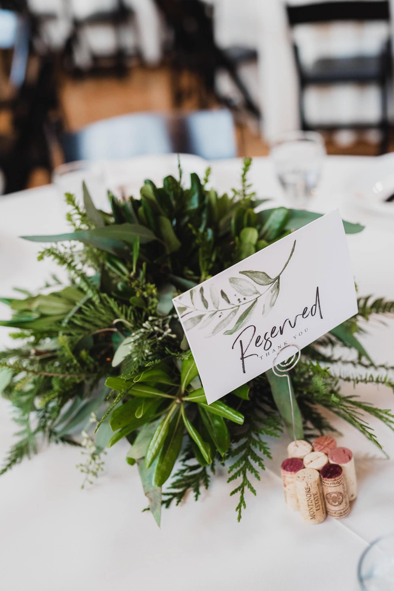 A centerpiece of green foliage with a Reserved sign on a table at the wedding at the Evergreen, decorated with wine corks.