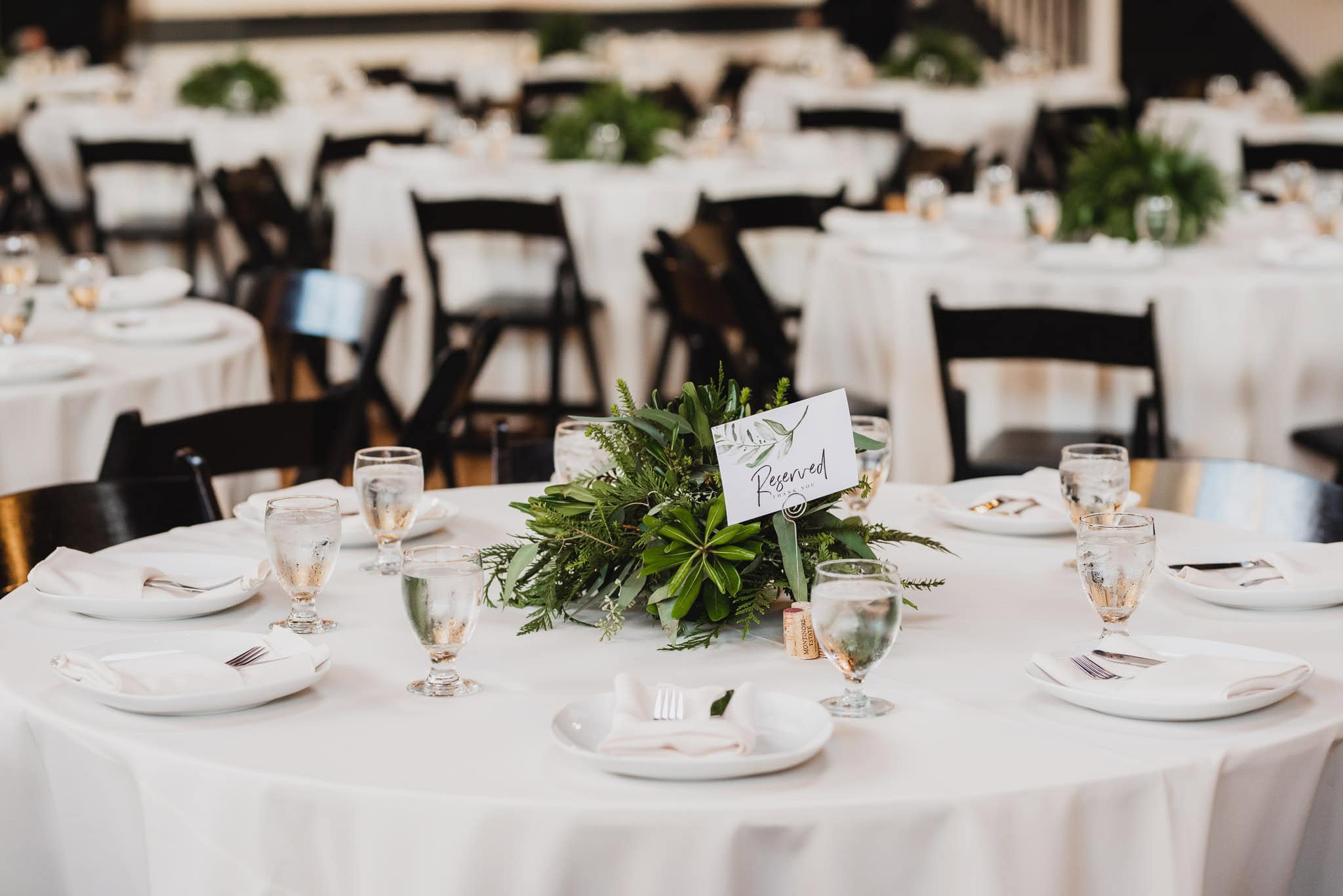 Round tables adorned with white tablecloths and green centerpieces are elegantly set for a formal event, with Reserved signs indicating a special wedding at the Evergreen.