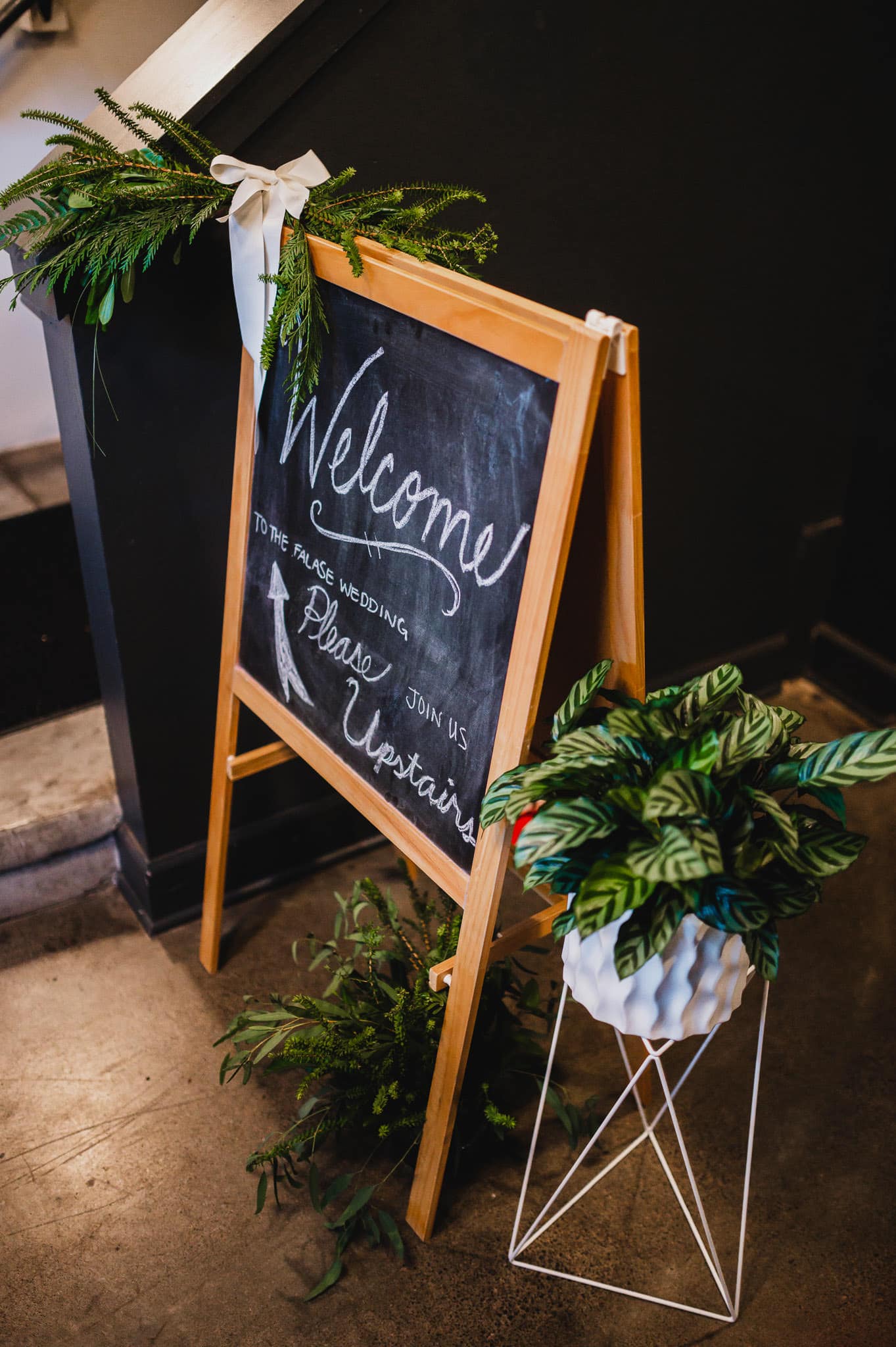 Wedding welcome sign artfully displayed on a chalkboard easel, surrounded by lush green plants, set the stage for a beautiful celebration at the Evergreen.