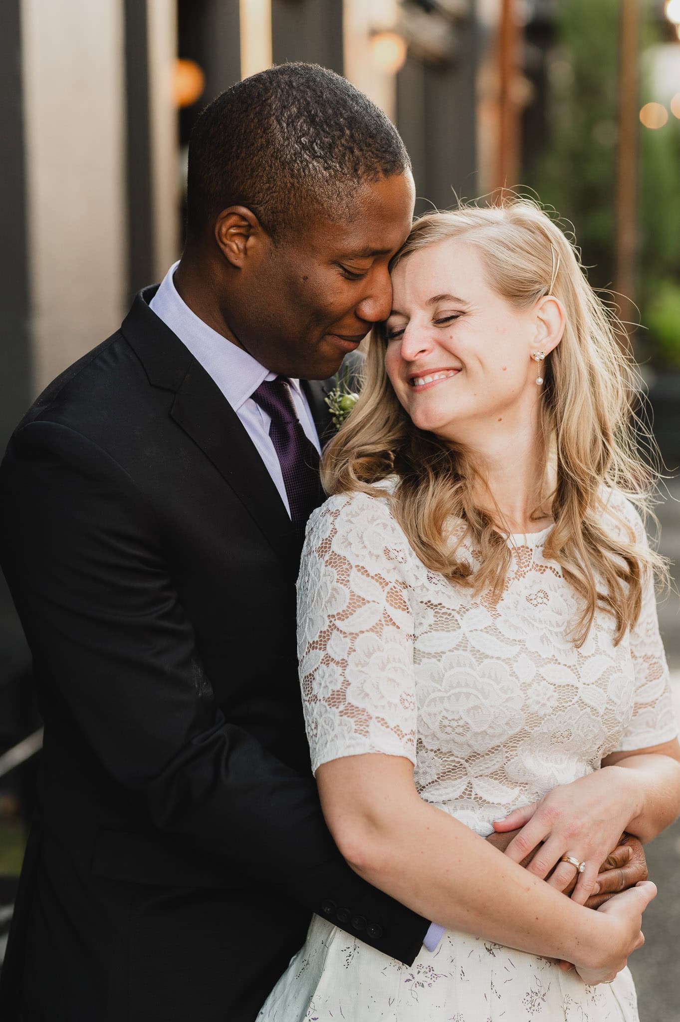 At the Evergreen, a couple embraces lovingly; the woman smiles with her eyes closed, basking in the special moment outdoors in formal attire.