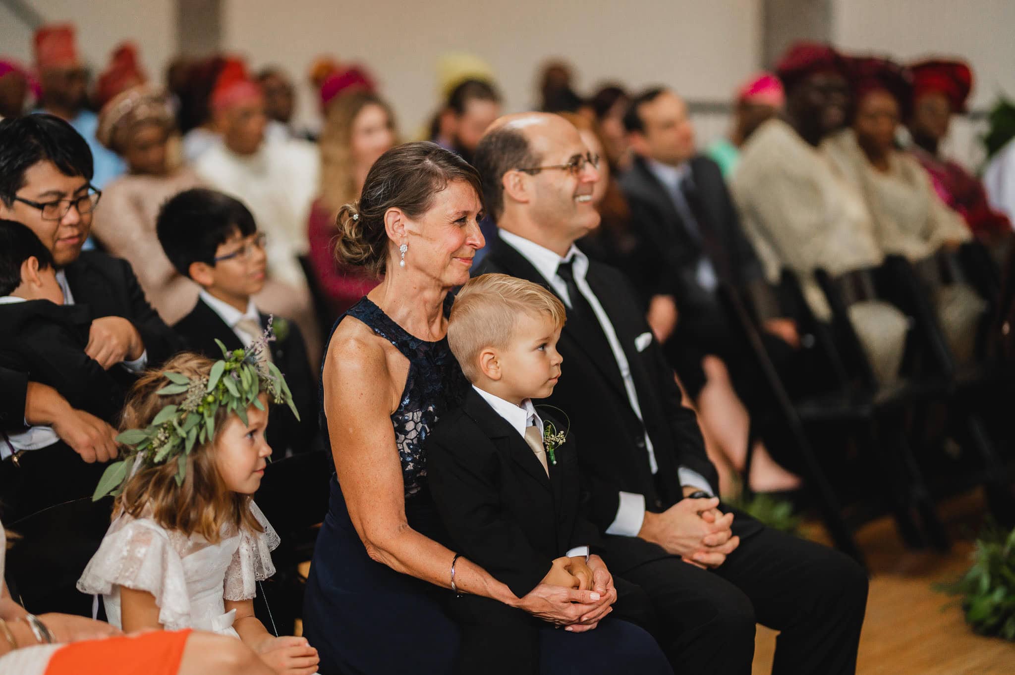 Guests, including children in formal attire, sit attentively during the indoor wedding at the Evergreen.