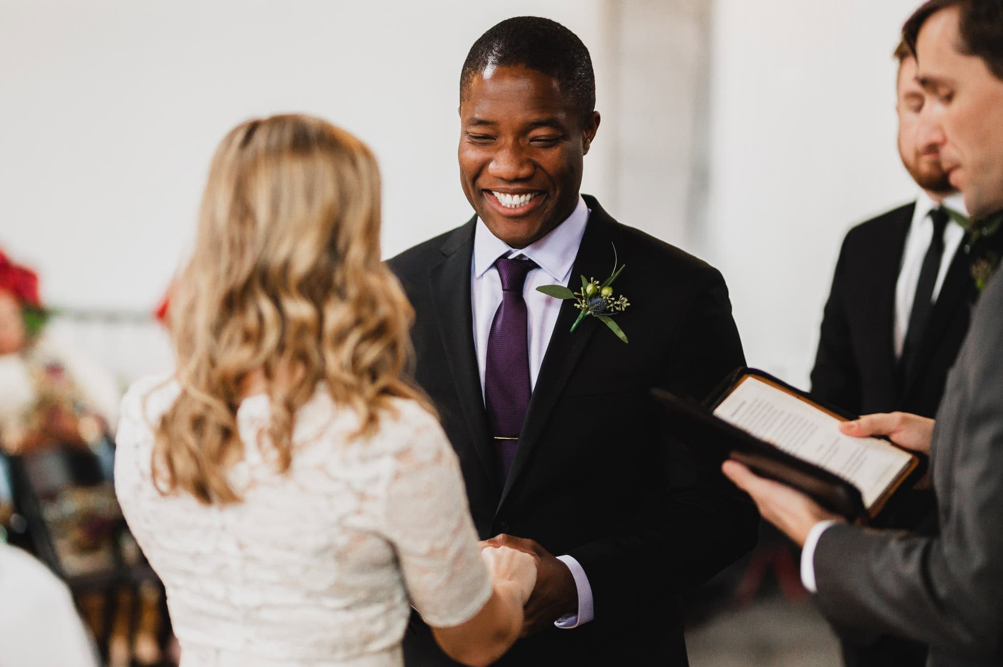 At their wedding at the Evergreen, a couple exchanges vows, the groom smiling as he holds the brides hands.