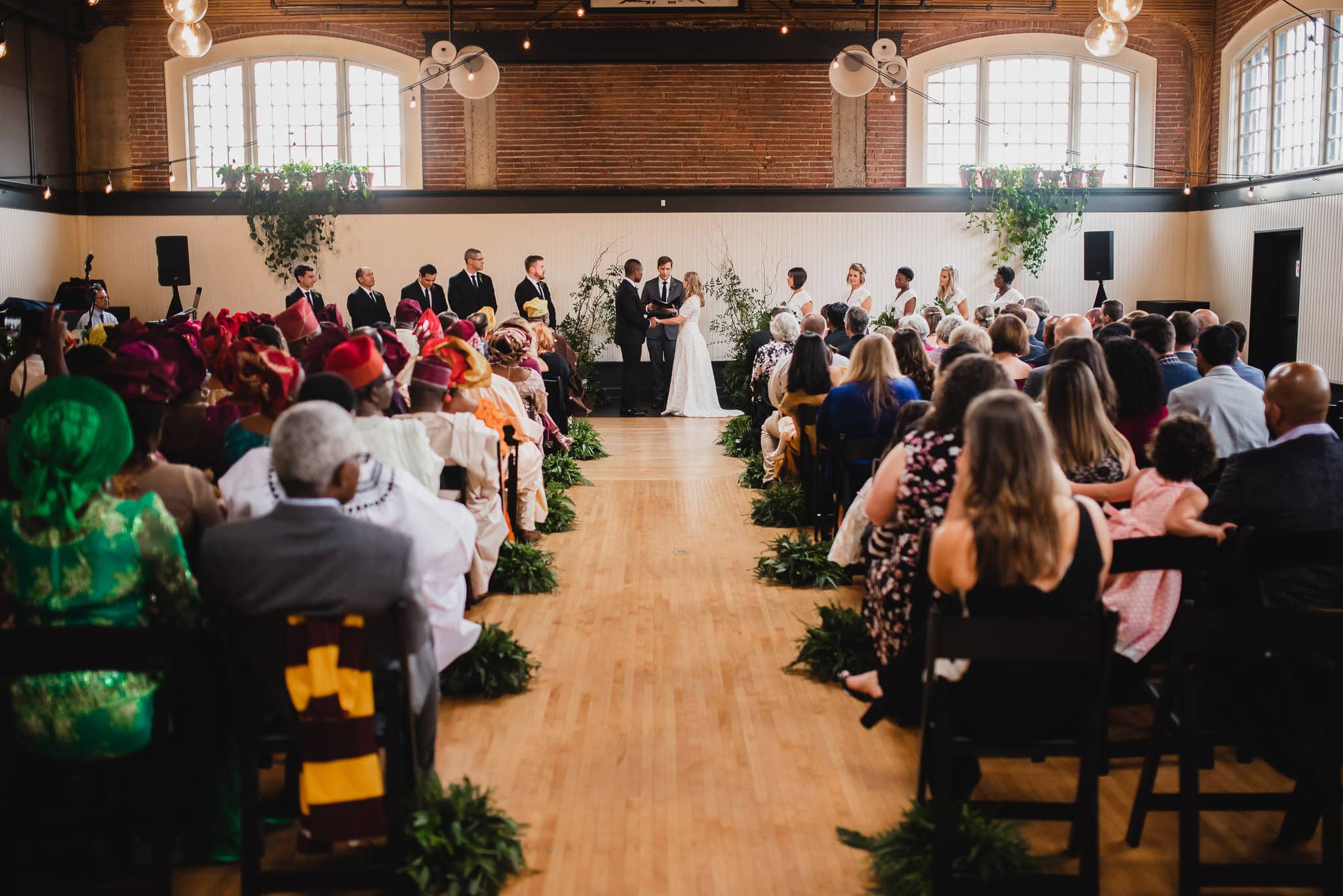 The wedding at the Evergreen featured a beautiful ceremony in a hall with guests seated on either side of the aisle, adorned with lush greenery.