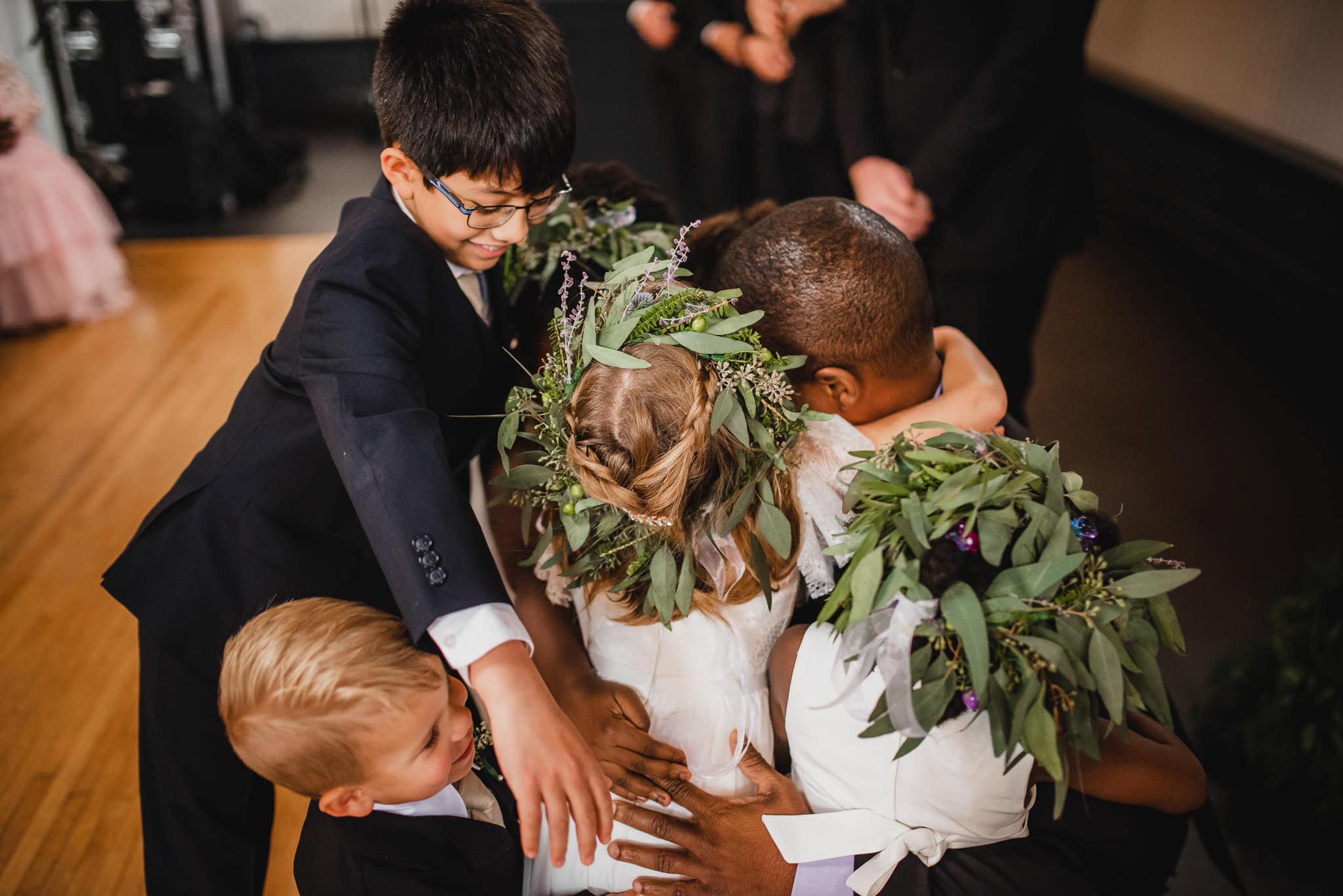 Group of children in formal attire hugging, with some wearing floral crowns, at a wedding at the Evergreen.