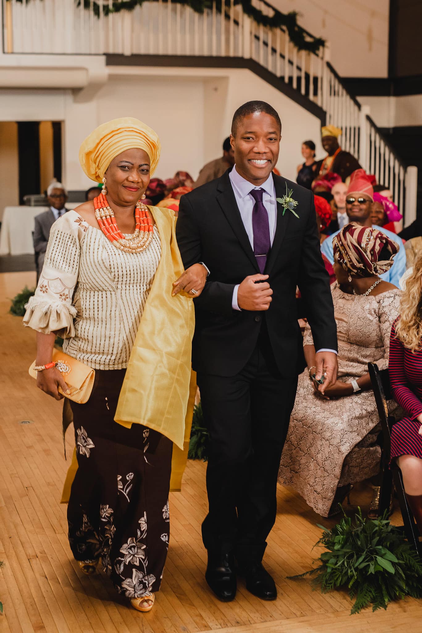 A woman in traditional attire and a man in a suit walk down the aisle, smiling, at a wedding at the Evergreen.