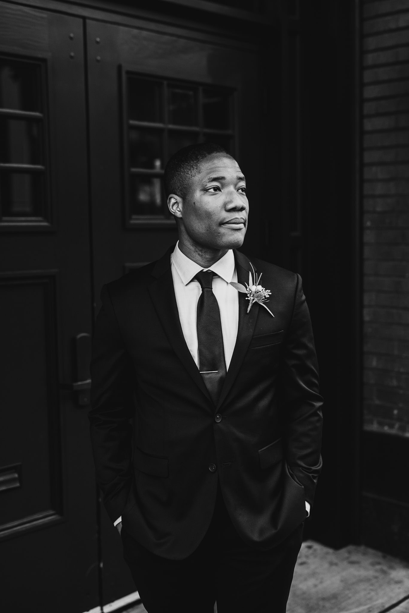A man in a suit with a floral boutonniere stands confidently with hands in pockets, gazing to the side during wedding portraits near The Evergreen.