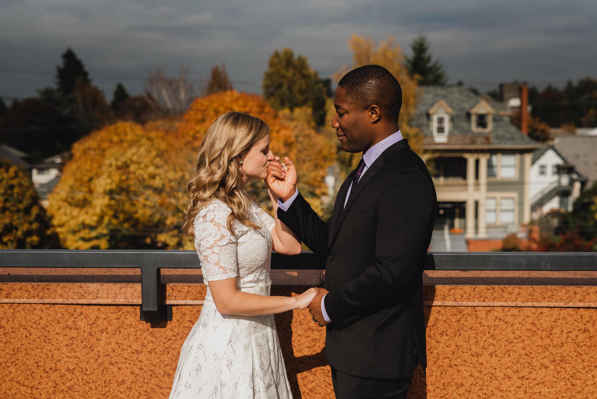 A couple stands on the rooftop of an Airbnb, sharing a tender first look before their wedding at The Evergreen. They hold hands, framed by autumn trees and cozy houses in the background.