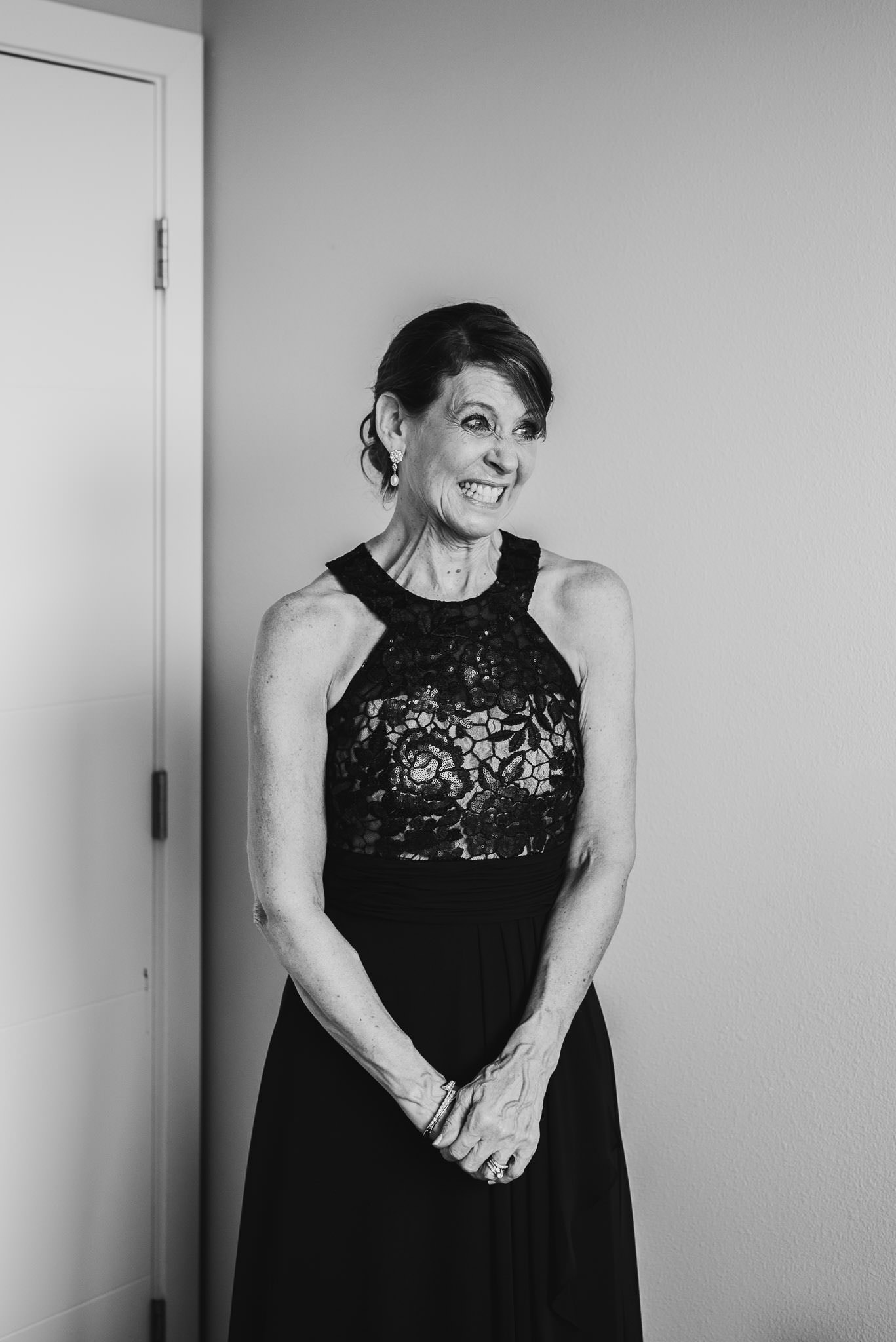 A woman in a lace dress smiles joyfully while standing by a door at an Airbnb rental, getting ready for a wedding at The Evergreen.