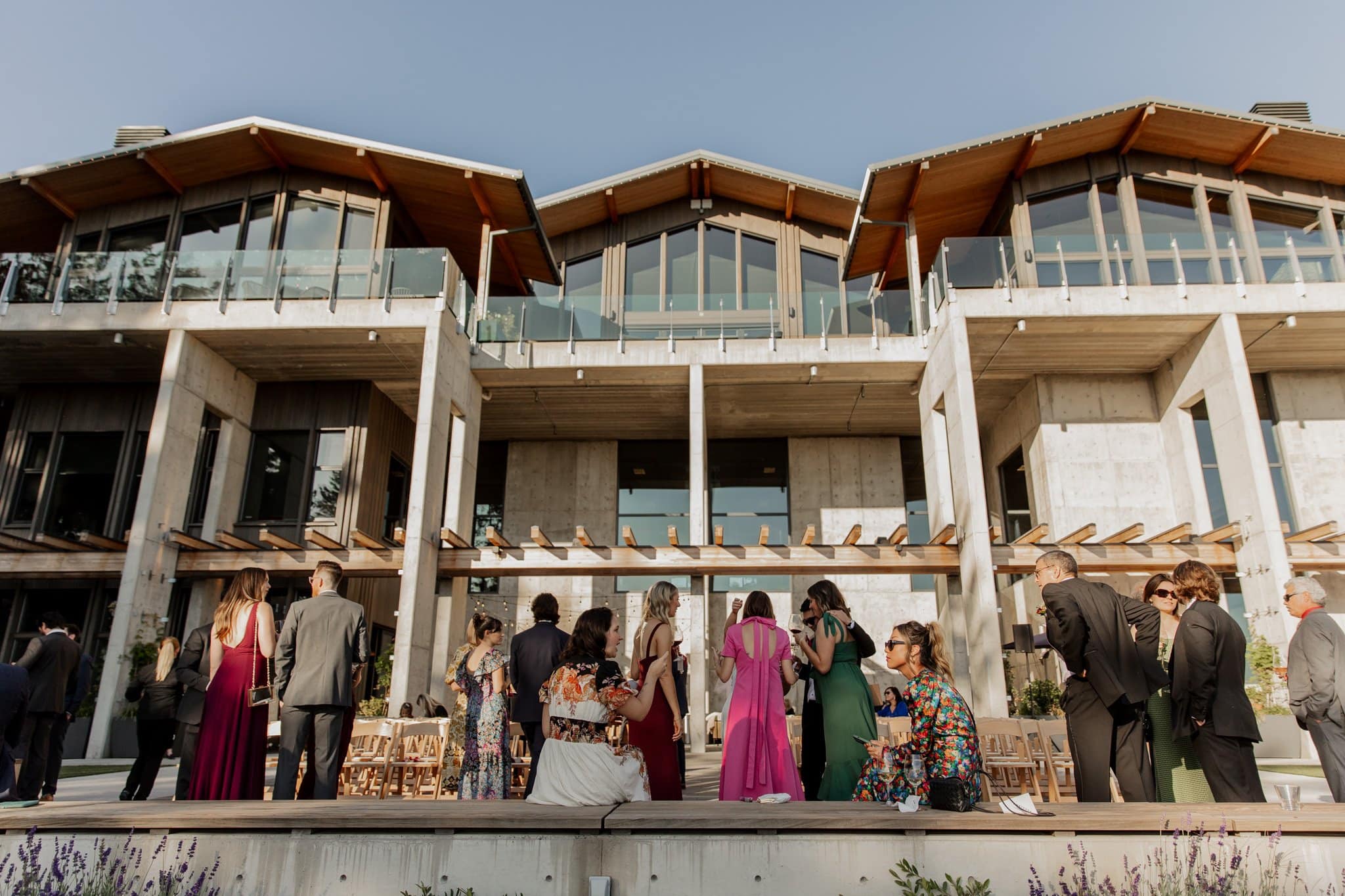 Guests in formal attire gather outside Amaterra Winery, a distinguished Portland wedding venue, under a clear sky and beside the large modern building.