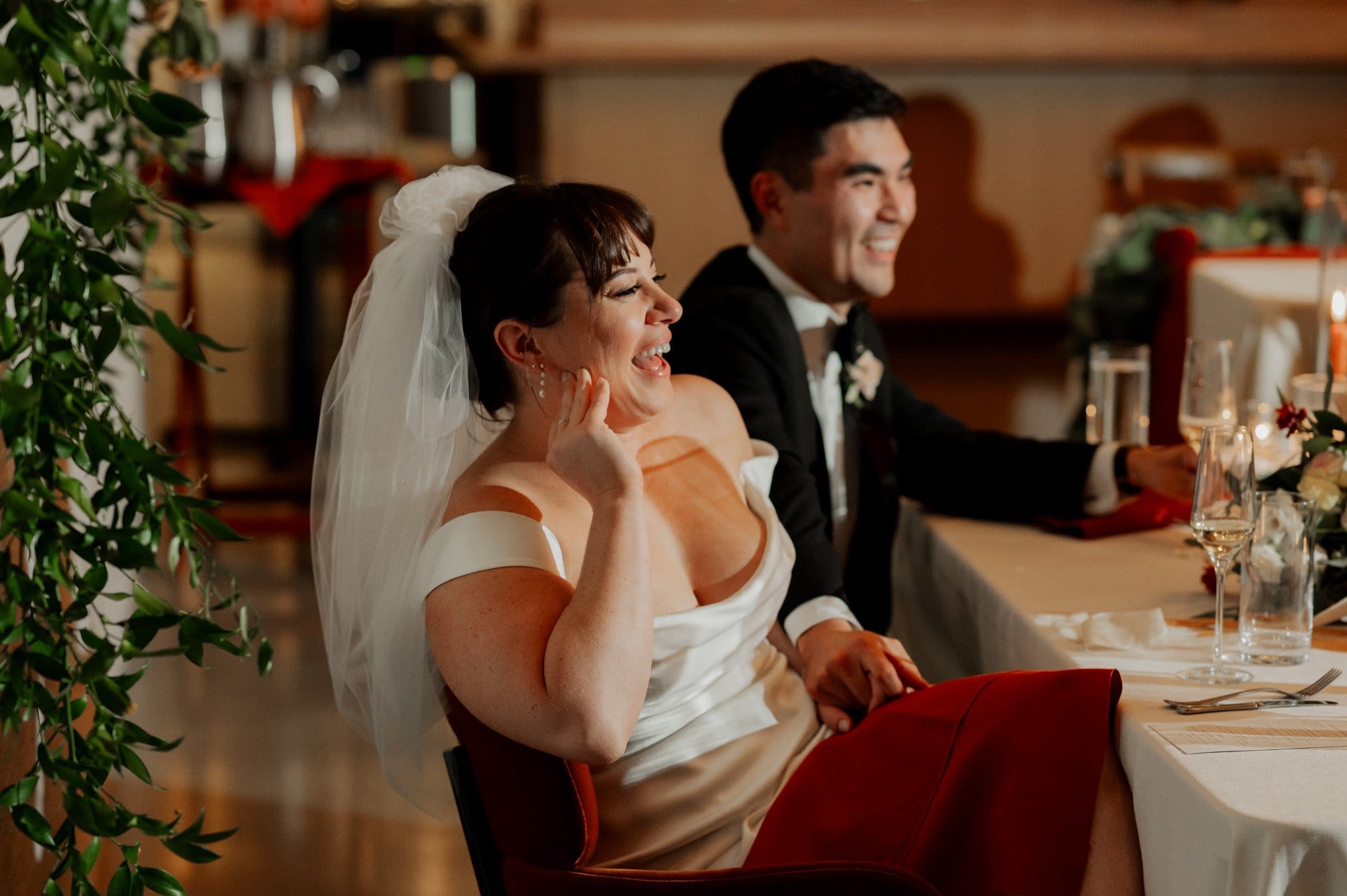 The bride in a white dress and groom in a suit share laughter at a decorated table during their wedding reception at the Skyline Ballroom, nestled within the beautiful Amaterra Winery, an elegant Portland wedding venue.