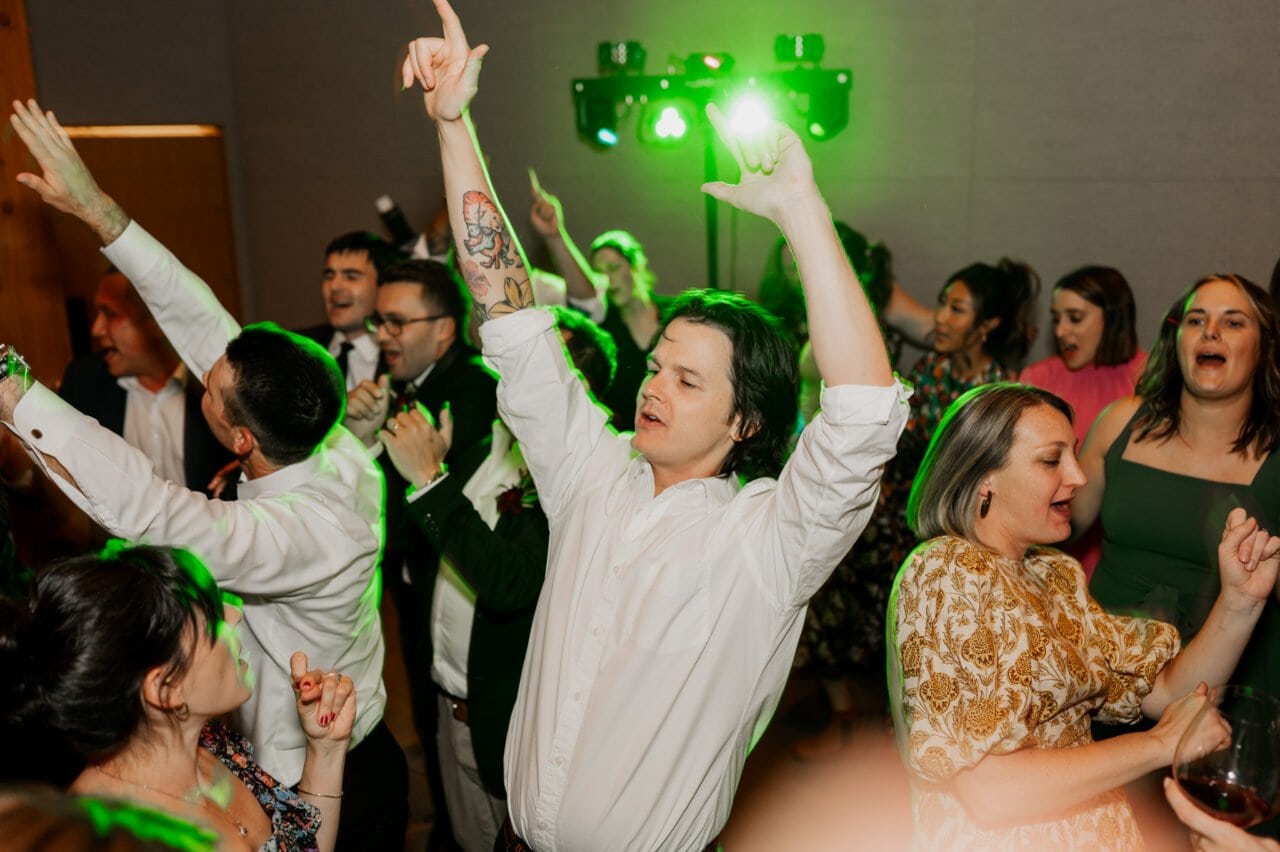People dancing energetically at a party with green lights in the background, reminiscent of vibrant Amaterra Winery wedding photos.