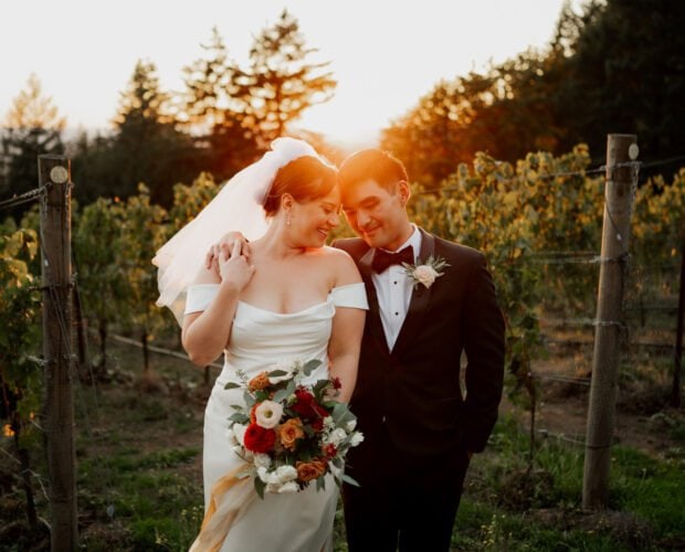 Bride and groom smiling at each other, standing in a vineyard at sunset at Amaterra Winery. She holds a bouquet of flowers, perfectly capturing the essence of their wedding photos.