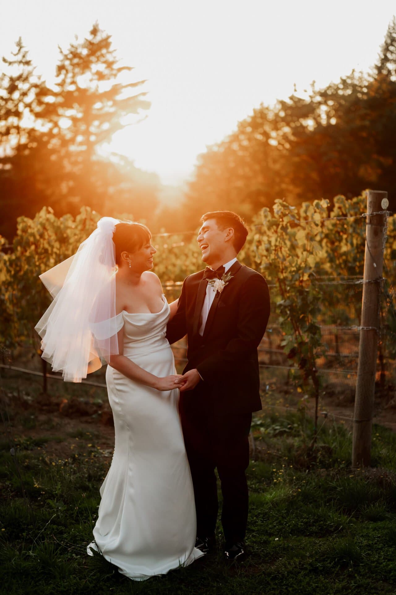 A bride and groom smile at each other in the golden light of sunset, surrounded by the lush vines of Amaterra Winery, perfectly capturing their weddings romantic essence.