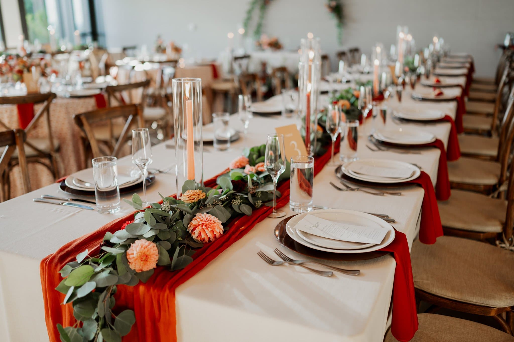 An elegant table setting inspired by Amaterra Winery wedding photos features red runners, floral garlands, candles, and neatly arranged plates and glasses.